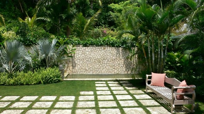 progettare giardino palme svariate muri pietra panchina legno