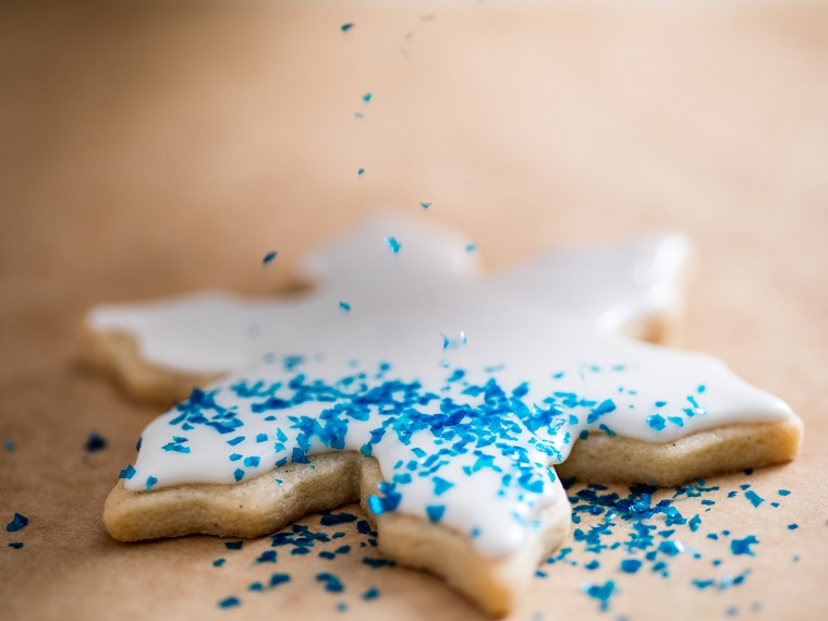 Ricette di Natale, biscotto forma fiocco di neve decorato con della glassa reale bianca e decorato con del glitter alimentare per dolci 