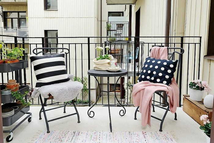 come-arredare-un-balcone-mobili-da-esterno-ferro-battuto-accenti-colore-cuscini-coperta-colore-rosa-carrello-piante