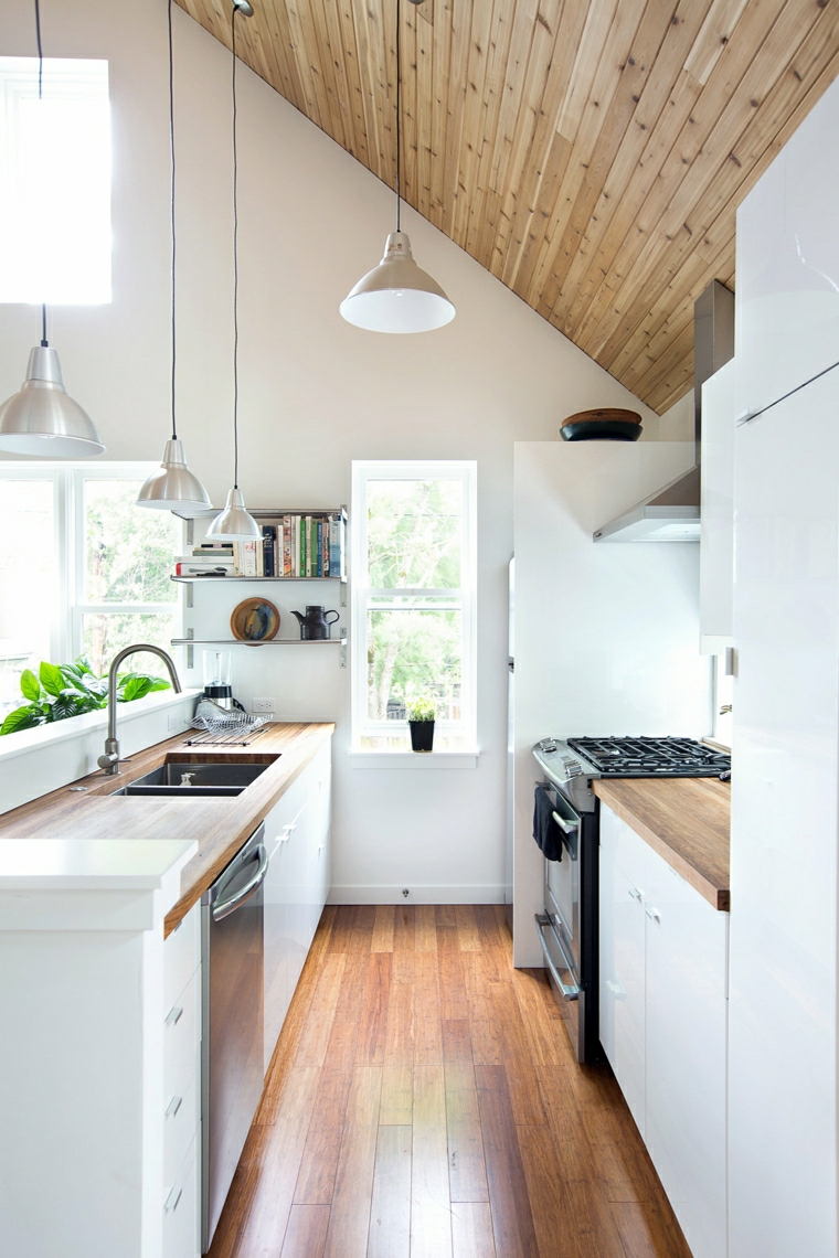 Cucina piccola in mansarda con soffitto in legno, le ante degli armadietti sono in legno di colore bianco 