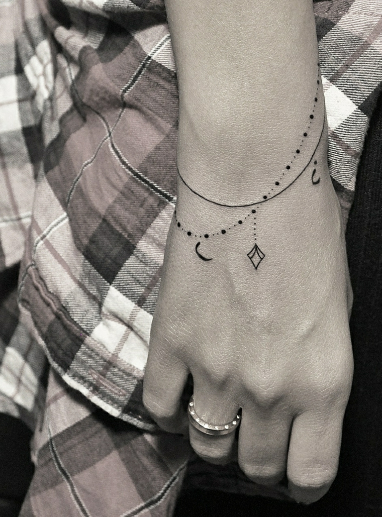 Tattoo tipo braccialetto di colore nero sulla mano di una ragazza con ciondoli 