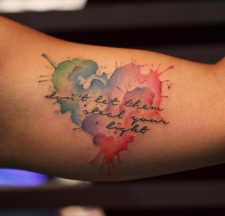 Tattoo particolari piccoli e femminili, idea con una scritta piccola e cuore intorno colorato a schizzi 