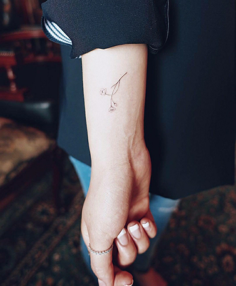 Tattoo di un piccolo fiore sul braccio di una ragazza 
