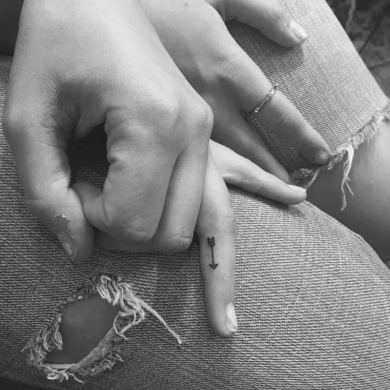 Idea carina per un tatuaggio femminile da fare sul dito anulare della mano, piccola freccia di colore nero 