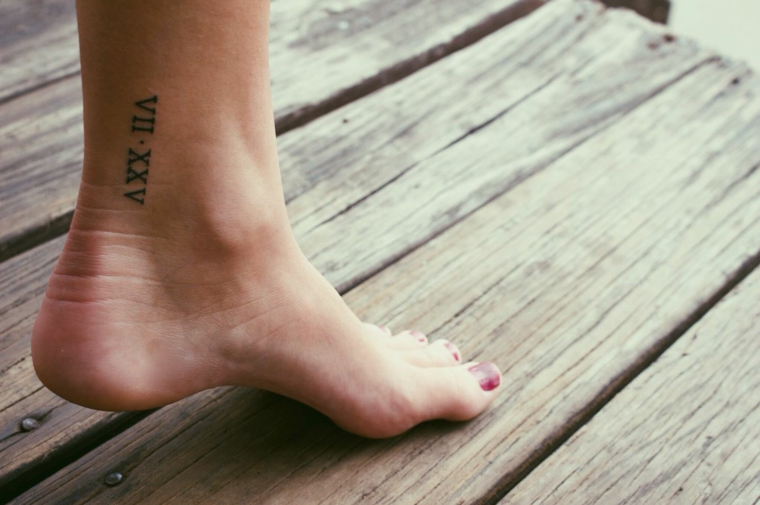 Tatuaggi piccoli caviglia, tattoo numeri romani, piede donna con unghie colorate di rosso