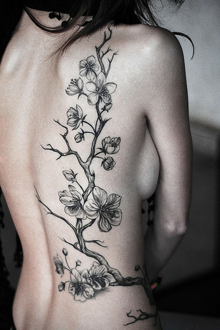 Albero fiorito sulla schiena di una donna, tattoo molto grande di colore nero con sfumature 