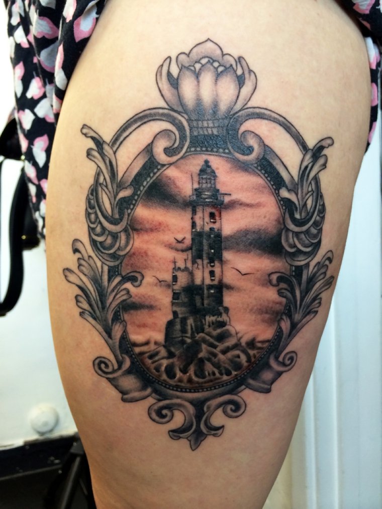 tattoo in bianco e nero sul braccio con un faro, un cielo nuvoloso e una cornice decorata
