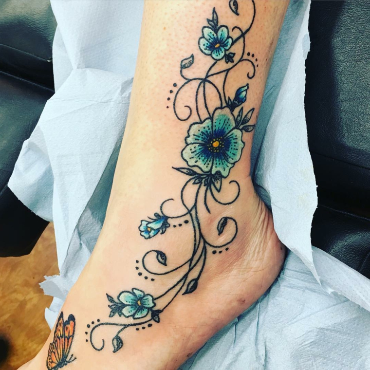 tatuaggio alla caviglia, un disegno raffigurante delle fiori azzurri e blu e delle farfalle gialle