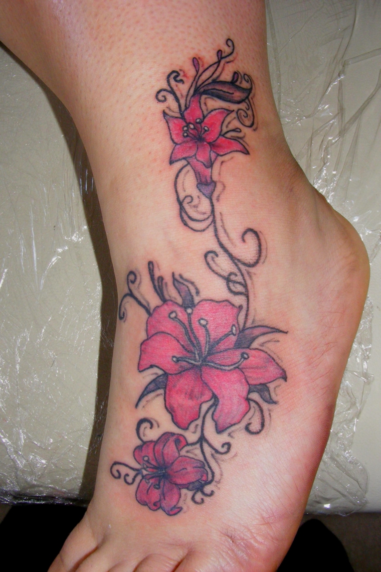 tatuaggio sulla caviglia, che comprende anche parte del piede con dei fiori di loto rossi