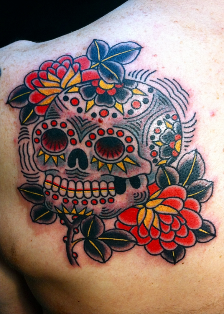 tatuaggi teschi messicani, un disegno colorato realizzato sulla spalla con due fiori sulle estremità
