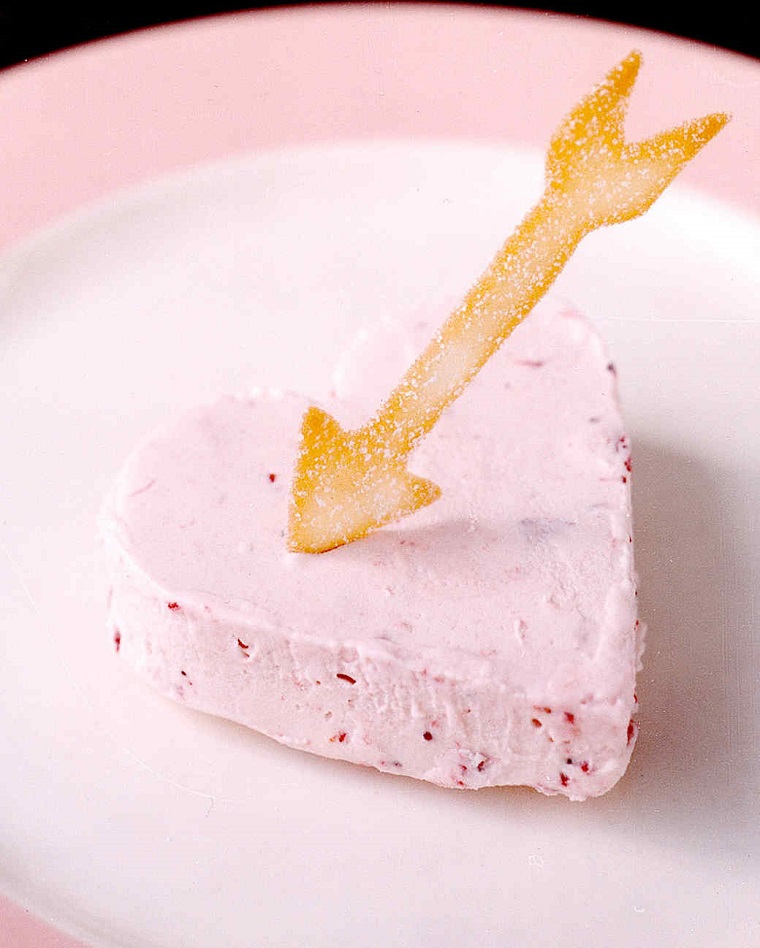 Cheesecake a forma di cuore e pezzettini di fragola, decorato con biscottino a forma di freccia 