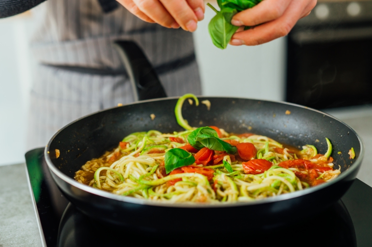 Spaghetti di verdure, padella con noodles di zucchine con pomodorini e foglie di basilico