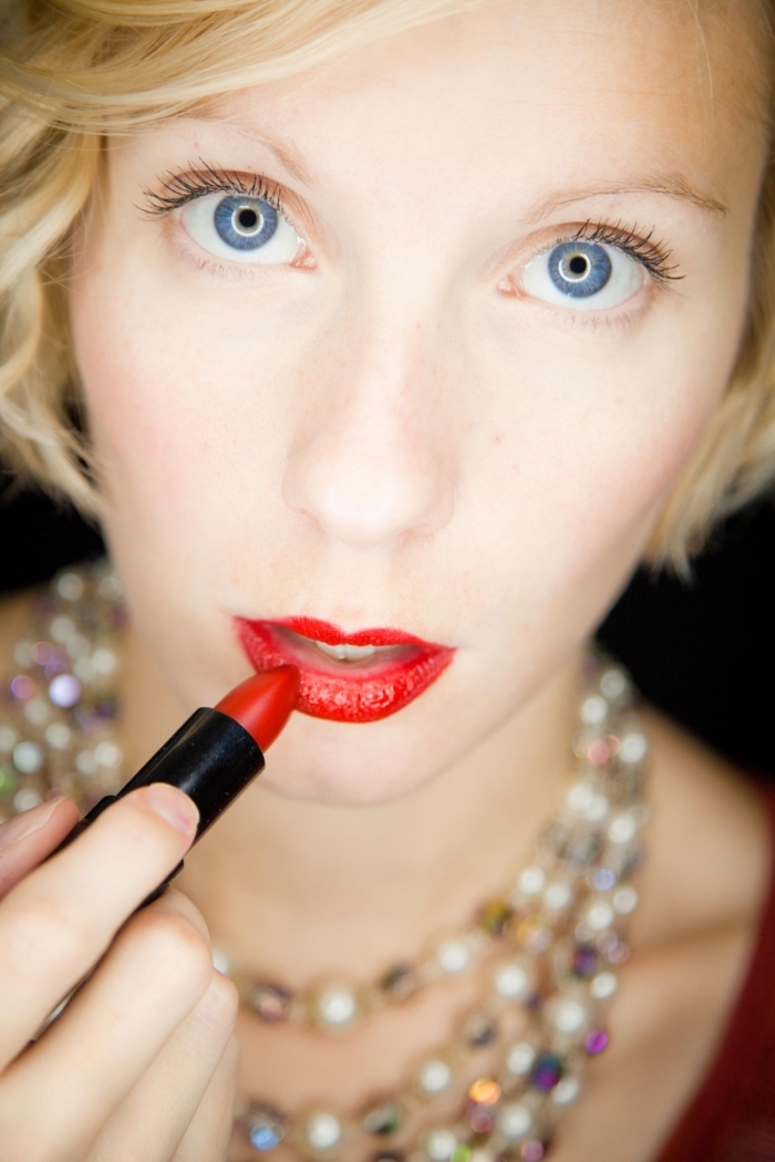 una ragazza bionda con gli occhi azzurri, labbra rosse e collana con delle perle