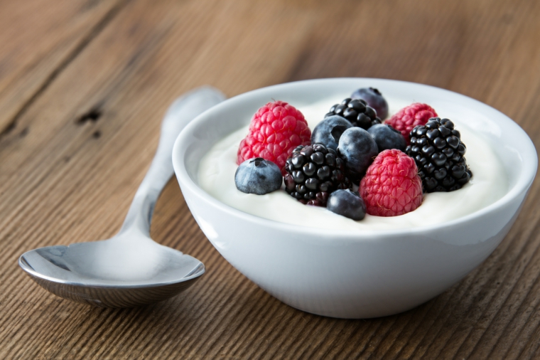 Ciotola con yogurt greco e frutti di bosco, cucchiaio su un tavolo di legno 