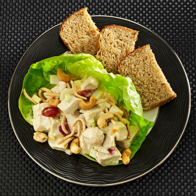 Idea per ricette dietetiche, piatto con insalata di pollo su una foglia di lattuga e fette di pane integrale 