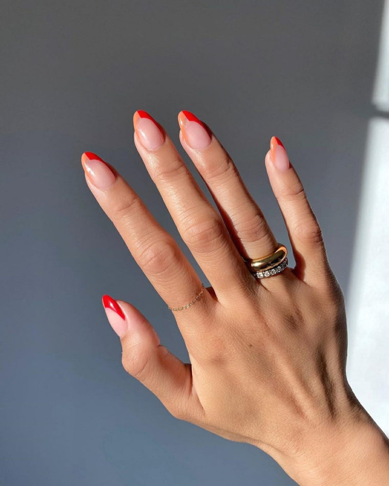 french manicure su unghie a mandorla di colore rosso e arancione donna con anelli sulle dita