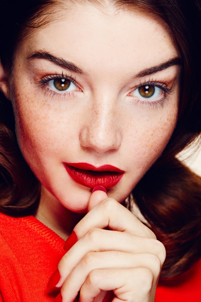 una ragazza con le lentiggini, un maglione, le unghie e le labbra della stessa tonalità di rosso