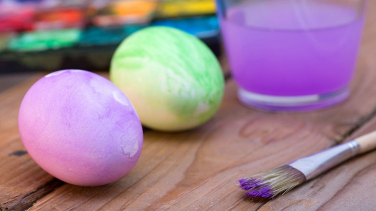 Uova di Pasqua dipinte a mano con pennello, colore viola e verde, tavolo di legno 