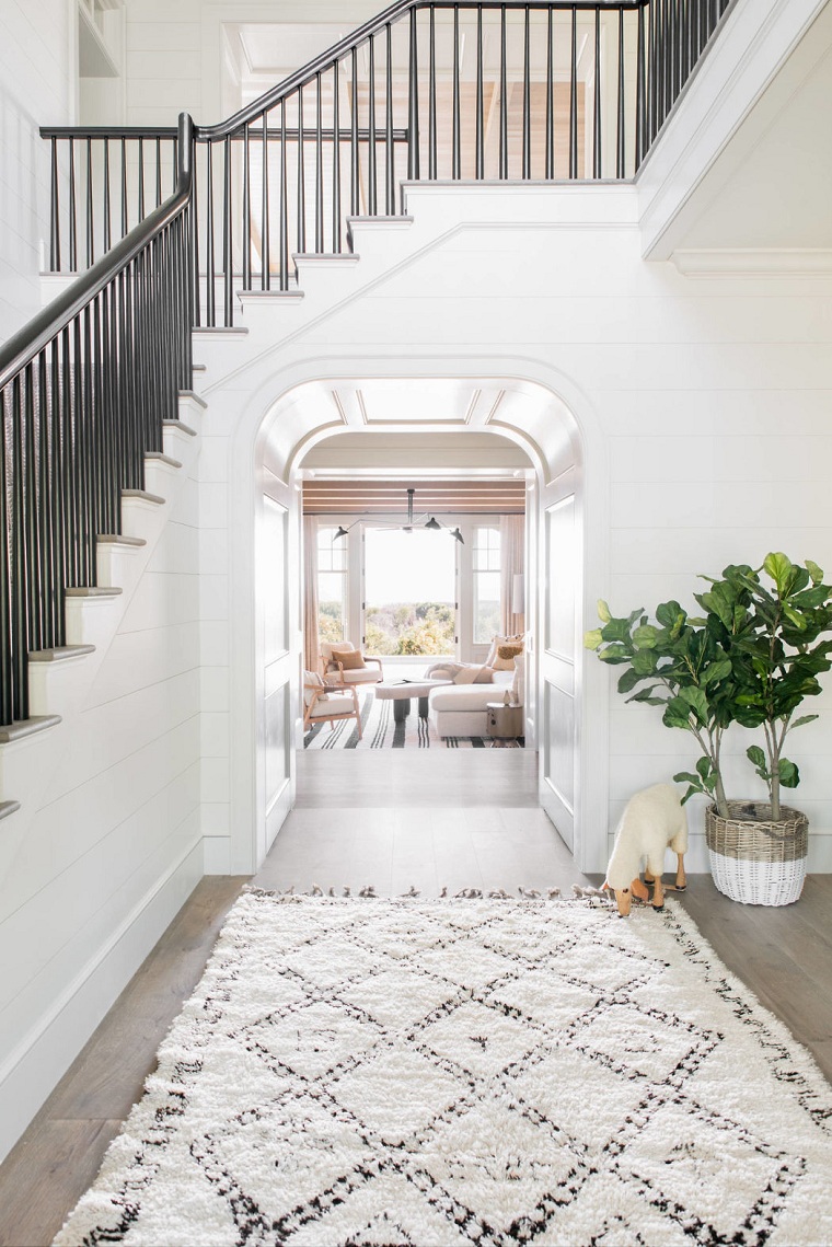 Ingresso di casa decorato, pavimento parquet colore grigio e tappeto, interni casa, decorazione con statuina cane e pianta in vaso di vimini 