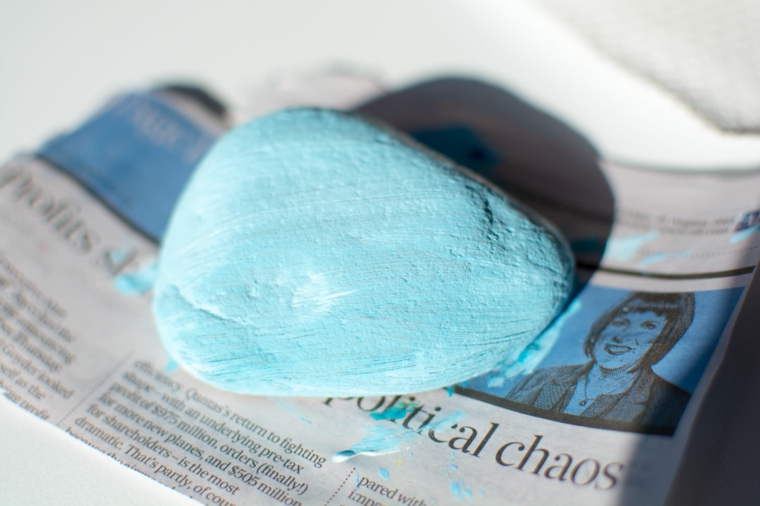 il sasso dipinto di azzurro che viene lasciato asciugare sulla carta di giornale: lavoretti per il papà