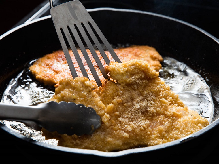 Secondi piatti estivi, cotoletta di pollo impannata e fritta in olio e burro, mestoli in acciaio 