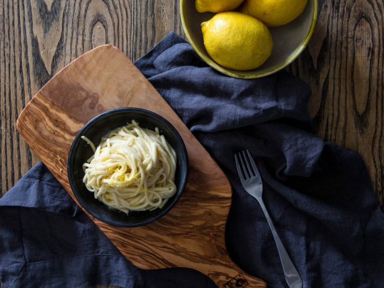 Cosa mangiare a cena, spaghetti al limone in ciotola rotonda di colore blu, tagliere di legno per servire 