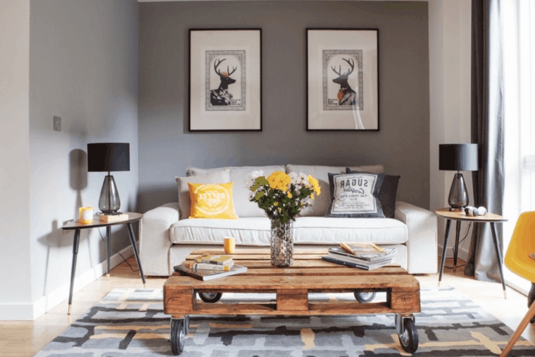 zona living moderna arredata con un divano bianco, tavolo in pallet, pareti tortora e accenti di giallo