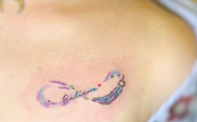 Simboli tattoo con infinito e piuma, scritta Believe al centro del tatuaggio