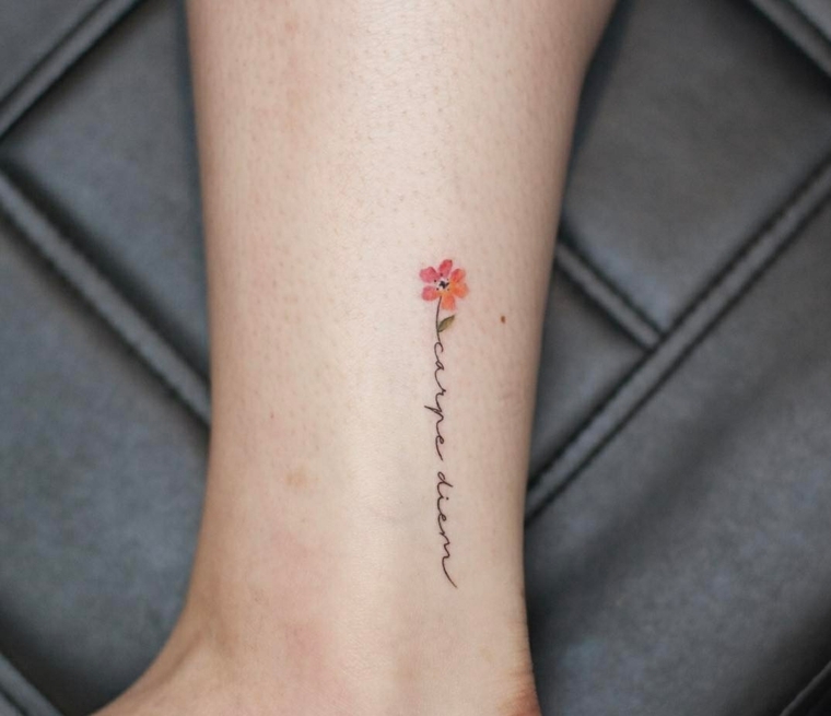 Scritta carpe diem sulla caviglia di una donna con piccolo fiore, tatuaggi sul piede femminile