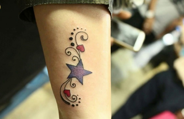 Tatuaggio stella significato e colorato di colore viola e cuori rossi sulla mano di una donna