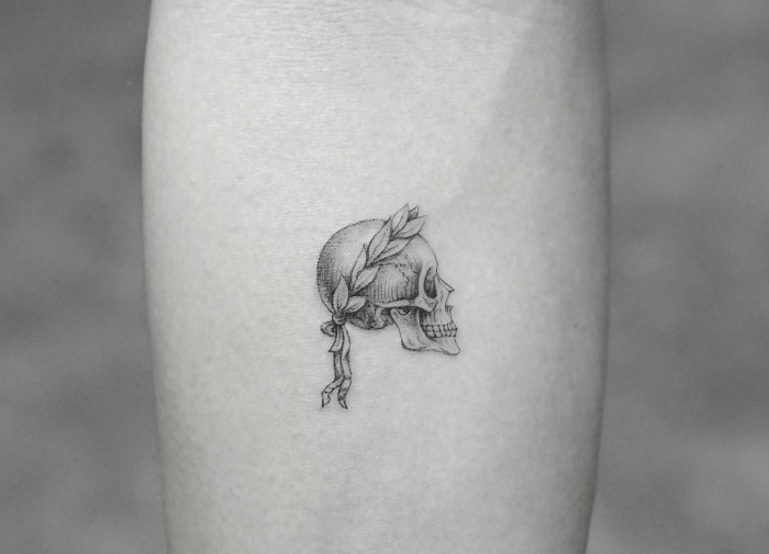 Il braccio di una donna tatuato con un cranio e corona floreale a treccia