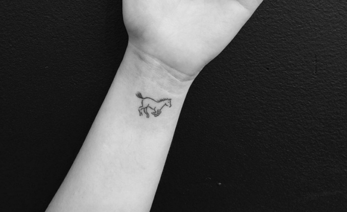 Il polso della mano con un piccolo tatuaggio e disegno di un cavallo che corre