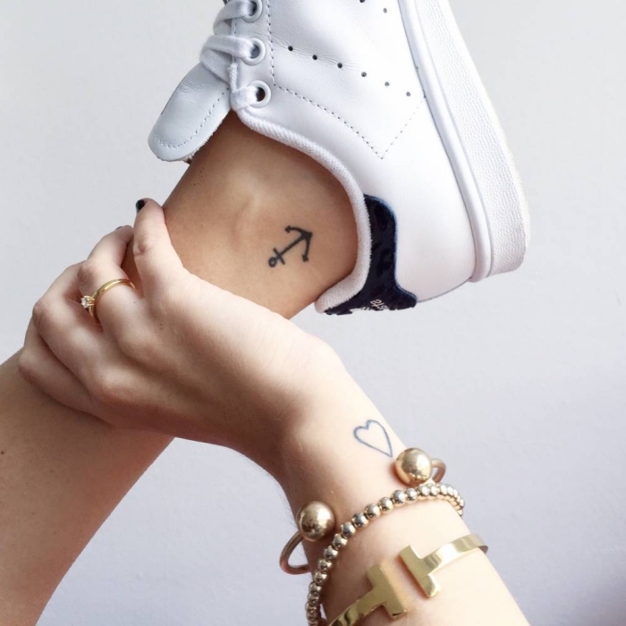 Donna con un tatuaggio ancora sulla caviglia, mano con tanti braccialetti di metallo