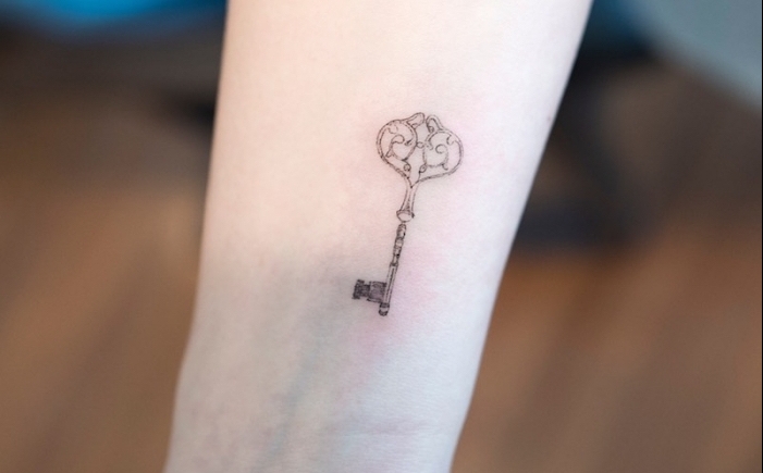 La mano di una donna tatuata con il disegno di una chiave vintage
