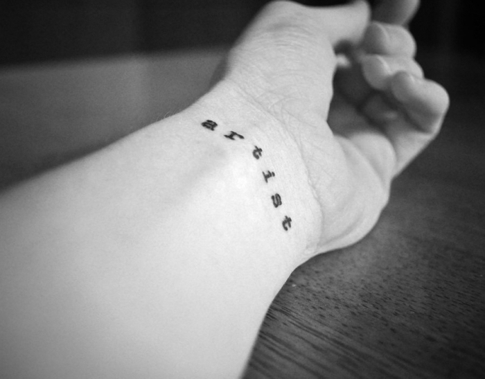 Tatuaggi piccoli e un'idea con scritta Artist sul polso della mano di una donna