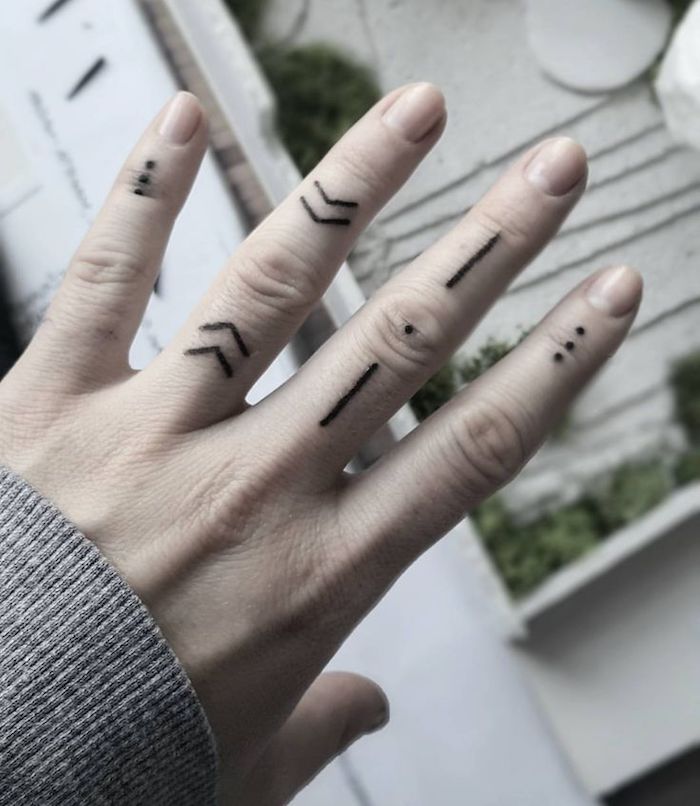 La mano di una dona con vari tatuaggi simbolici sulle dita
