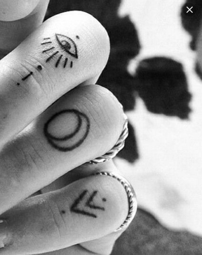 Mano di una donna con tatuaggi simboli sulle dita con occhio, luna e frecce con puntini