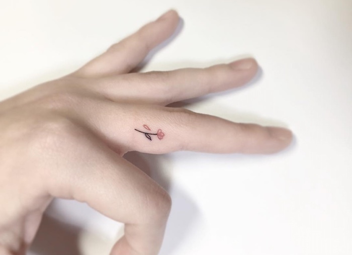 Tatuaggio sul dito medio di una donna con una piccola rosa colorata