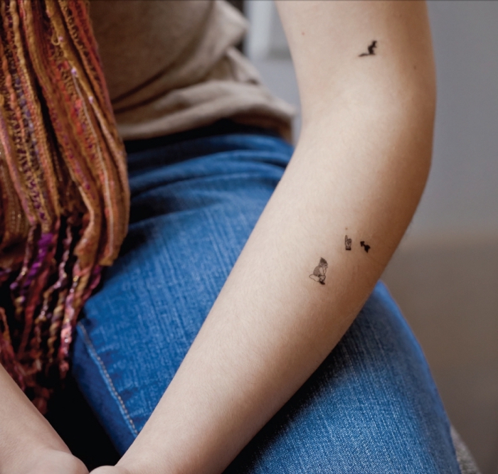 Il braccio di una donna tatuato con delle piccole figurine
