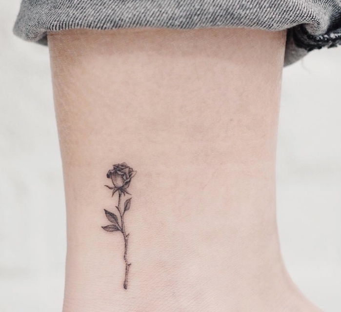 La caviglia di una donna tatuata con un disegno di rosa in bianco e nero con sfumature 