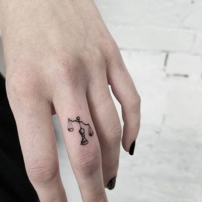 Idea per dei tatuaggi piccoli sulle mani, una bilancia sul dito medio di una donna