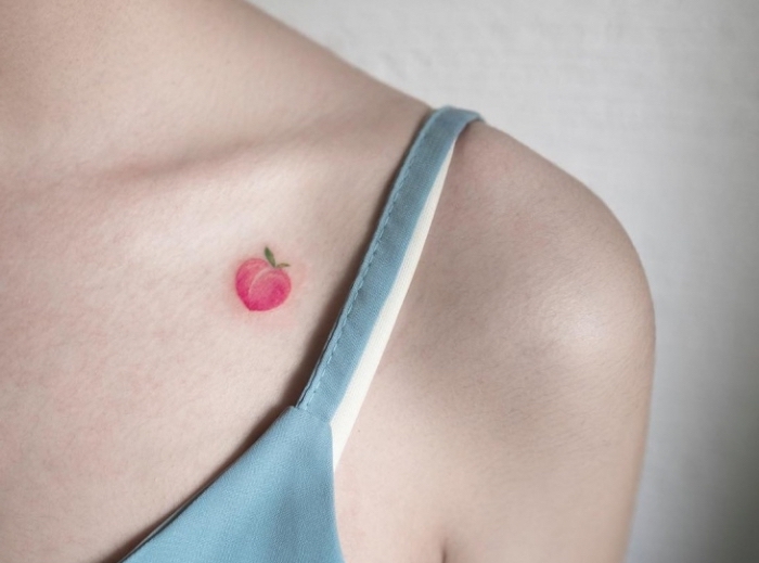 Una piccola pesca di colore rosa tatuata sulla spalla di una donna