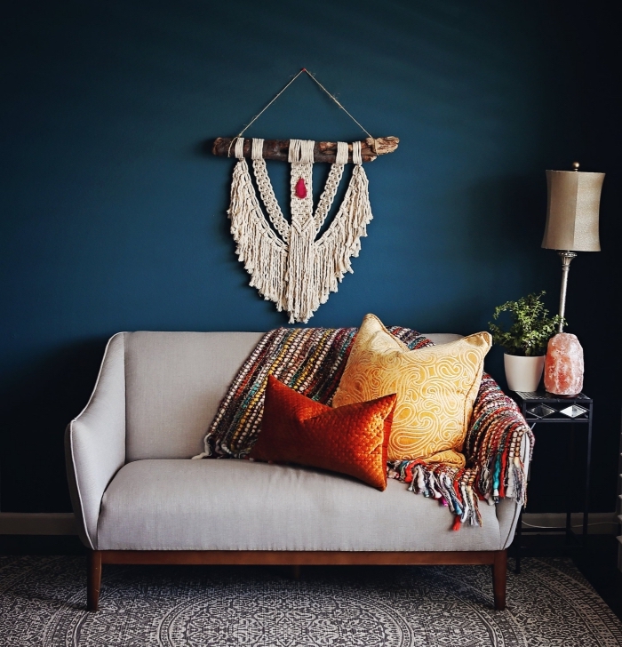 Salotto con parete di colore blu e divano grigio, decorazione rustica con macramè frange