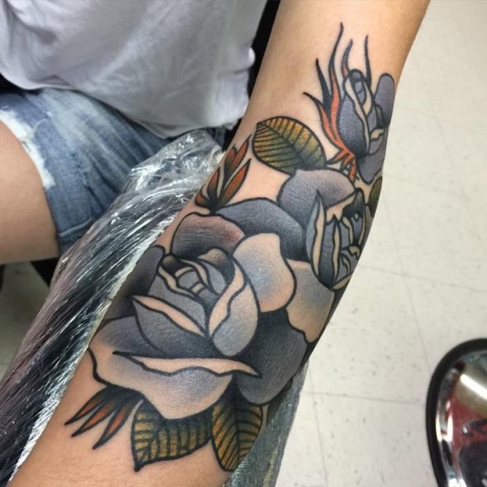 Il braccio di una donna con il disegno colorato di fiori con le foglie 