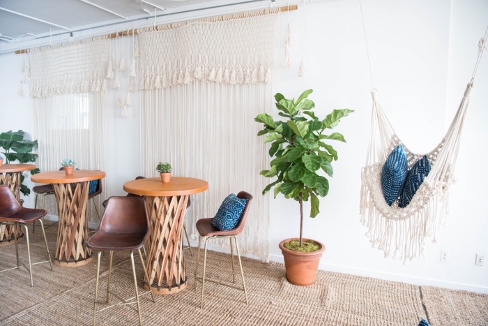 Un soggiorno con tavoli alti di legno e tende in macramè con corda bianca