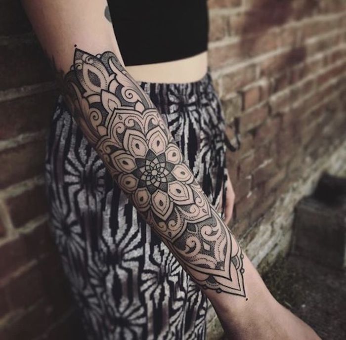 Tatuaggio mandala sul braccio di una donna, ragazza con pantalone palazzo e top nero
