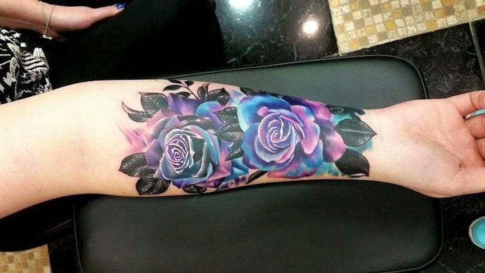 Tattoo fiori di colore rosa blu sul braccio di una donna con foglie nere