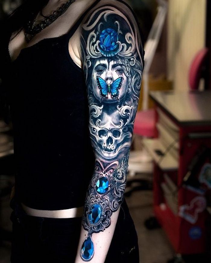 Idea per dei tatuaggi femminili sul braccio con disegni di farfalle e diamanti colorati di blu