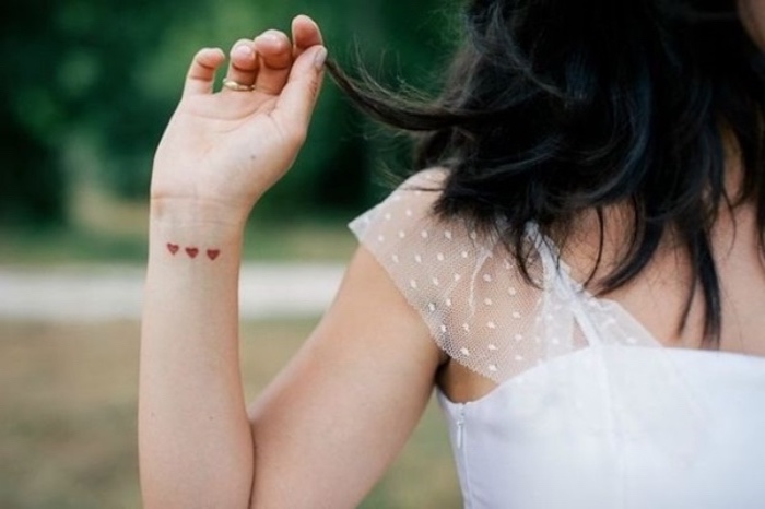 Tre cuori rossi, tatuaggi sul polso, donna con maglietta bianca