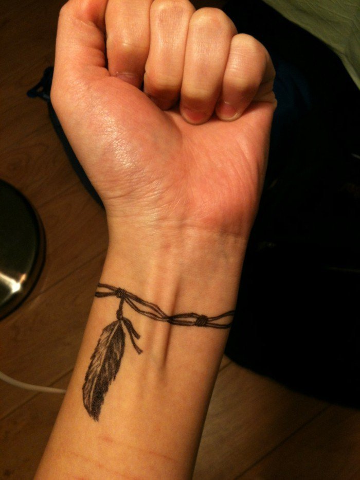 Tattoo piuma con braccialetto, tatuaggio polso della mano, uomo con pugno